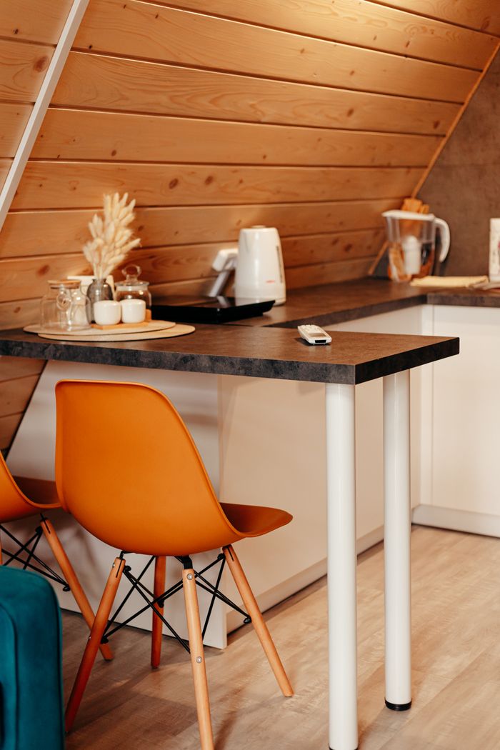 Warm and inviting modern kitchen with slanted wood ceiling, orange chairs, and countertop appliances.