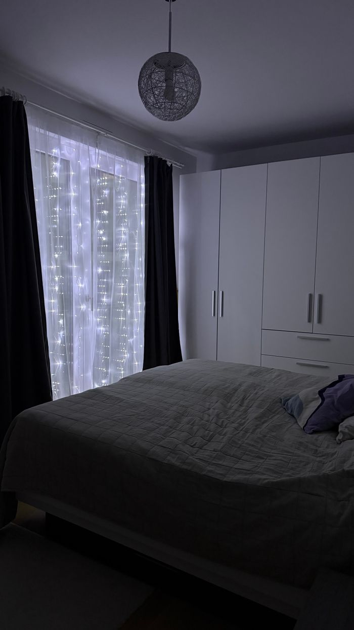 A dimly lit bedroom with twinkling fairy lights on the window, creating a cozy festive atmosphere.